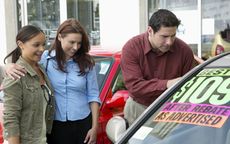 Parents looking at car on forecourt with daughter, smiling