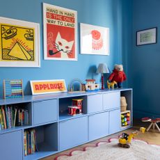 A blue-painted family living room with colourful wall art and tonal sideboard for toy storage