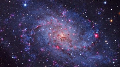 A image of a swirling galaxy and stars with pinks, blues and brooding colors