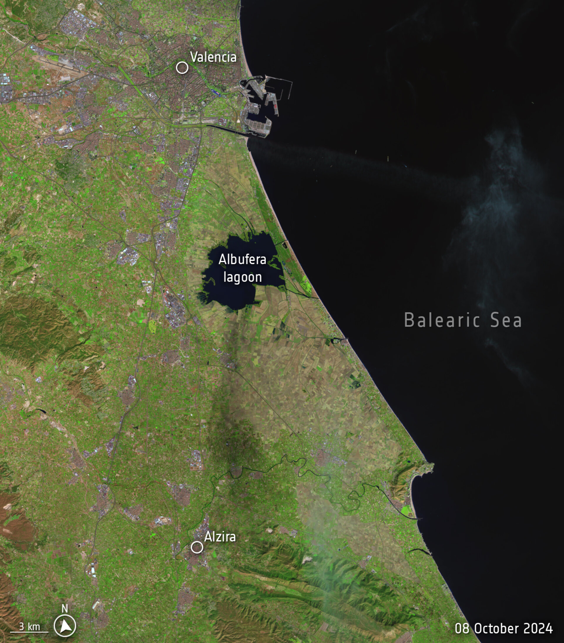 Aerial view from a high altitude, with green land on the left and the Balearic Sea on the right.