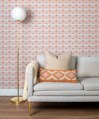 Geo wallpaper in coral and orange behind gray sofa with orange coordinating rectangular cushion.
