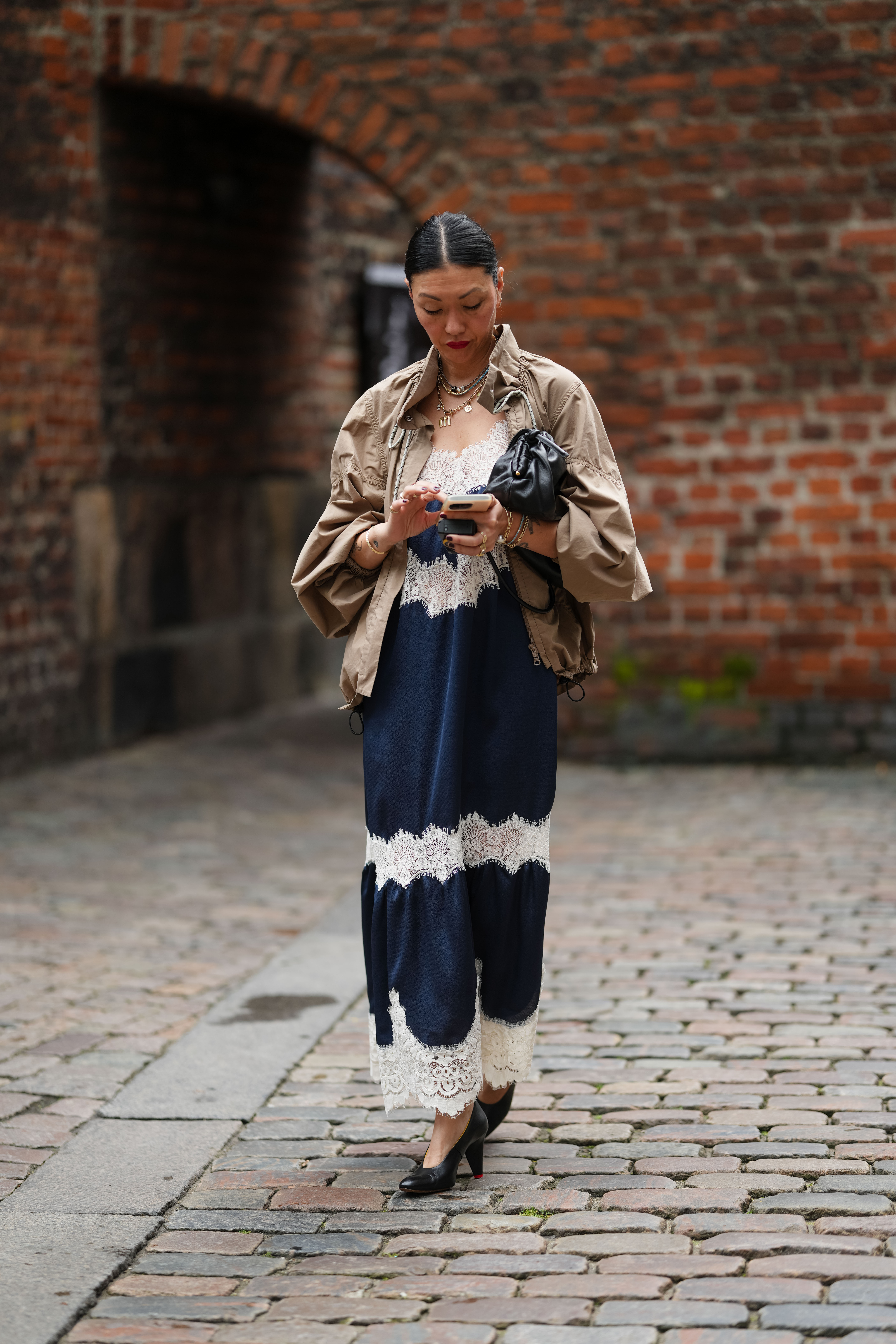 a woman wearing a khaki jacket over a navy and cream lace-trim dress in street style