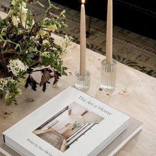 The Art of Home by Shea McGee on a coffee table with two candles and a floral arrangement
