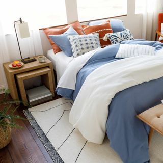 A cream rug with a black crack effect sits on top of a bed with white and blue sheets
