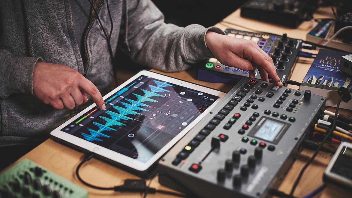 A man uses an iPad on a desk to record music with a synthesizer