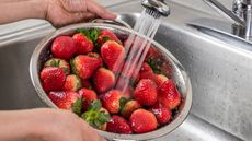 A silver colander full of strawberries being rinsed