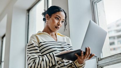 A woman looks at her open laptop while walking through her office building.