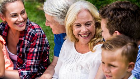 Happy family enjoying during picnic at park. Grandparents, adult children and grandchildren sit together in a candid shot.