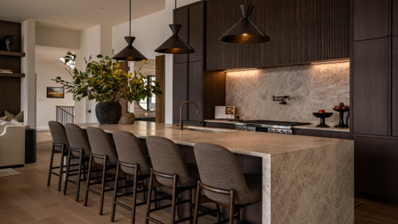 a dark toned, modern kitchen with a large leathered marble kitchen island with three pendant lights hanging above