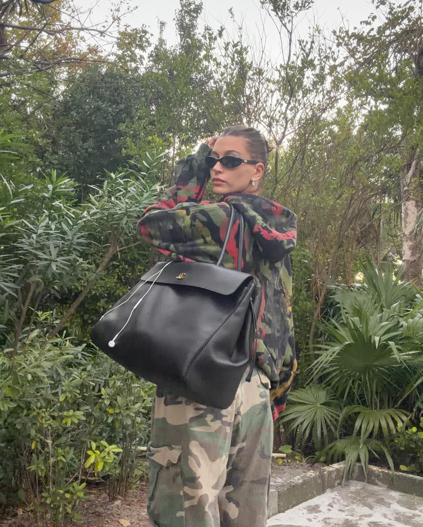Hailey wears a camouflage sweatshirt, camouflage pants, and a black tote bag in L.A.