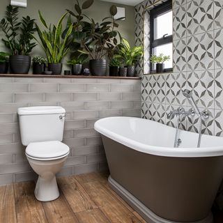 Bathroom with brown bathtub and shelf with pot plants and grey wall tiles