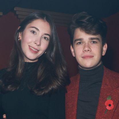 Samuel Chatto wears a red jacket and black top as he poses with girlfriend Eleanor Ekserdjian