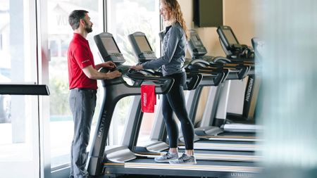 A trainer and woman talking in a gym on the running machine