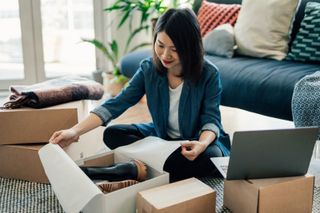 Young woman using laptop and packing packages, fulfilling online orders. E-commerce and online shopping helps small business. Working from home concept.