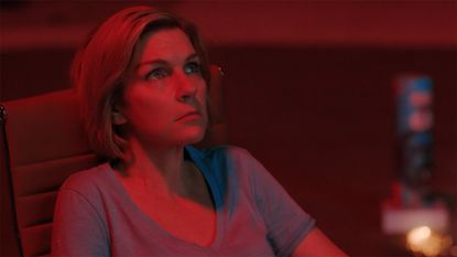Carol sitting down and bathed in red light from a firework at night in Pluribus episode 7