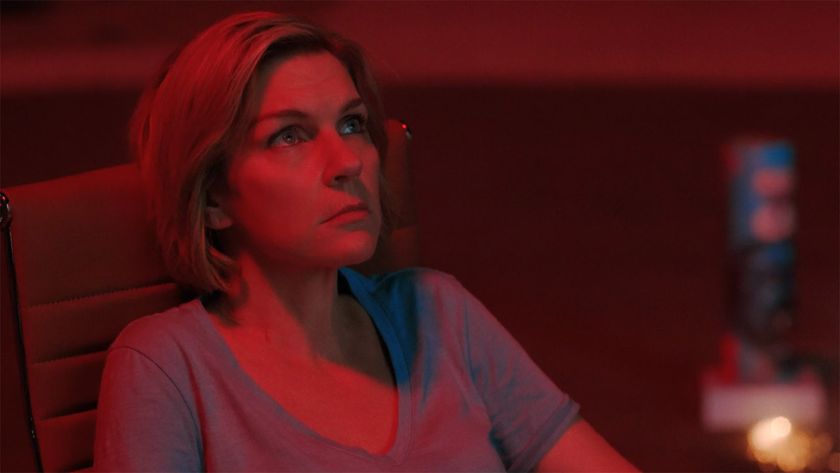 Carol sitting down and bathed in red light from a firework at night in Pluribus episode 7