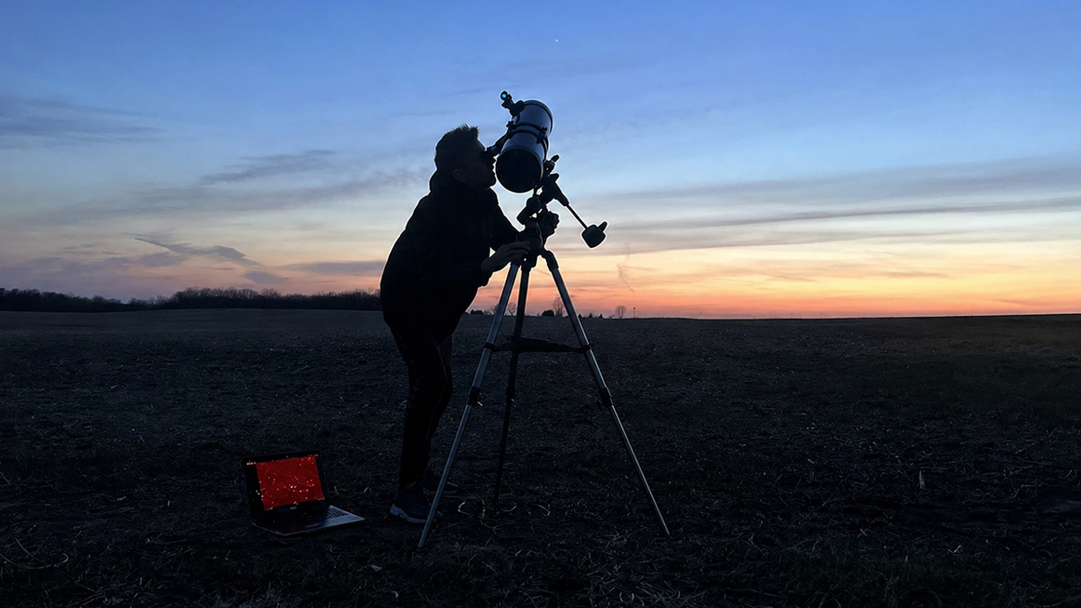 A man looking through a telescope at night. 