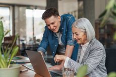 Older determined employee learning to work with new software, younger manager helping. Portrait of two colleagues in various age groups in office. Age diverse team concept.