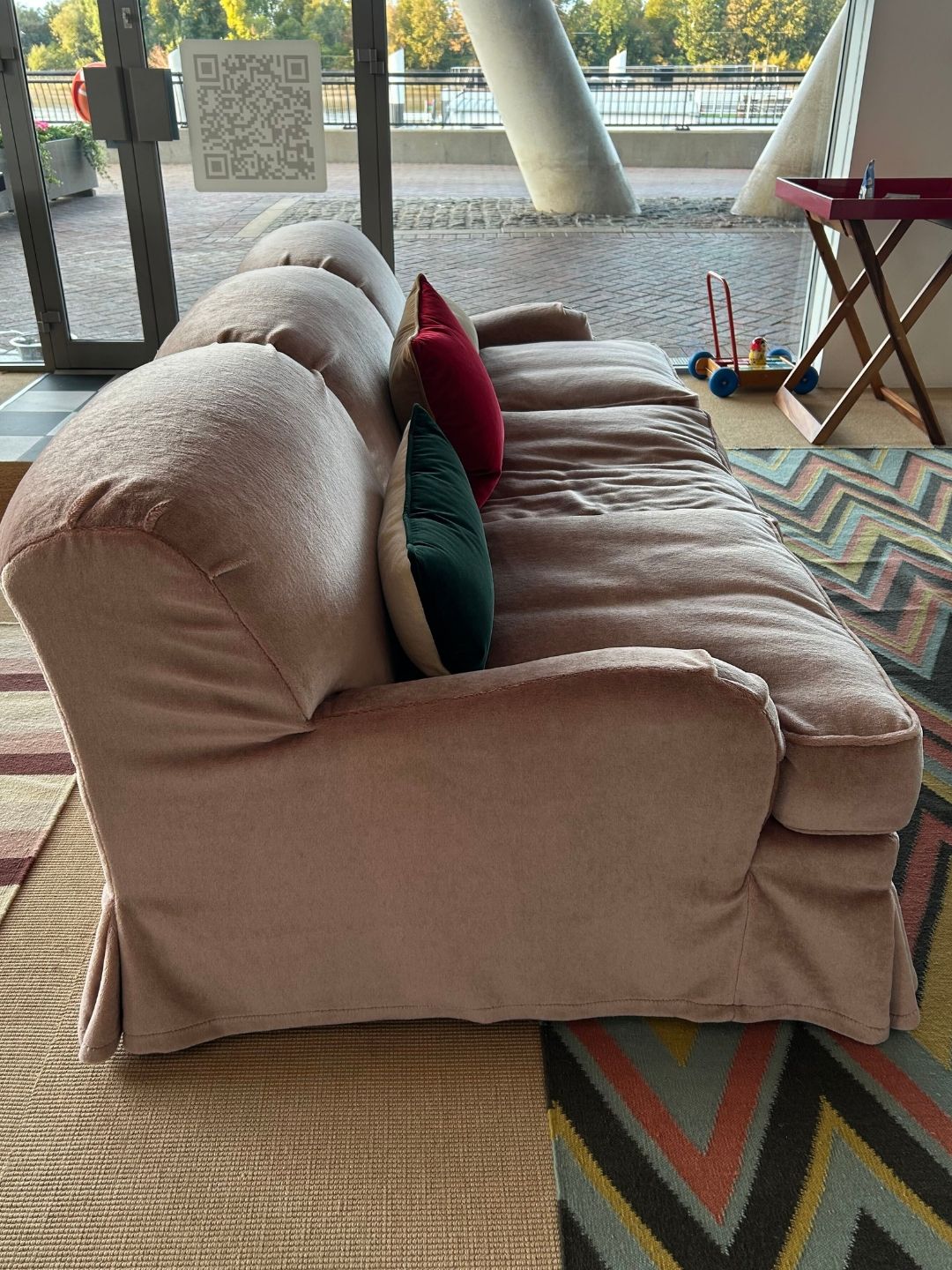 Side profile of the Lenny sofa in Heather Mohair Velvet, showing its rounded arm, deep cushions, skirted base and colourful scatter cushions.