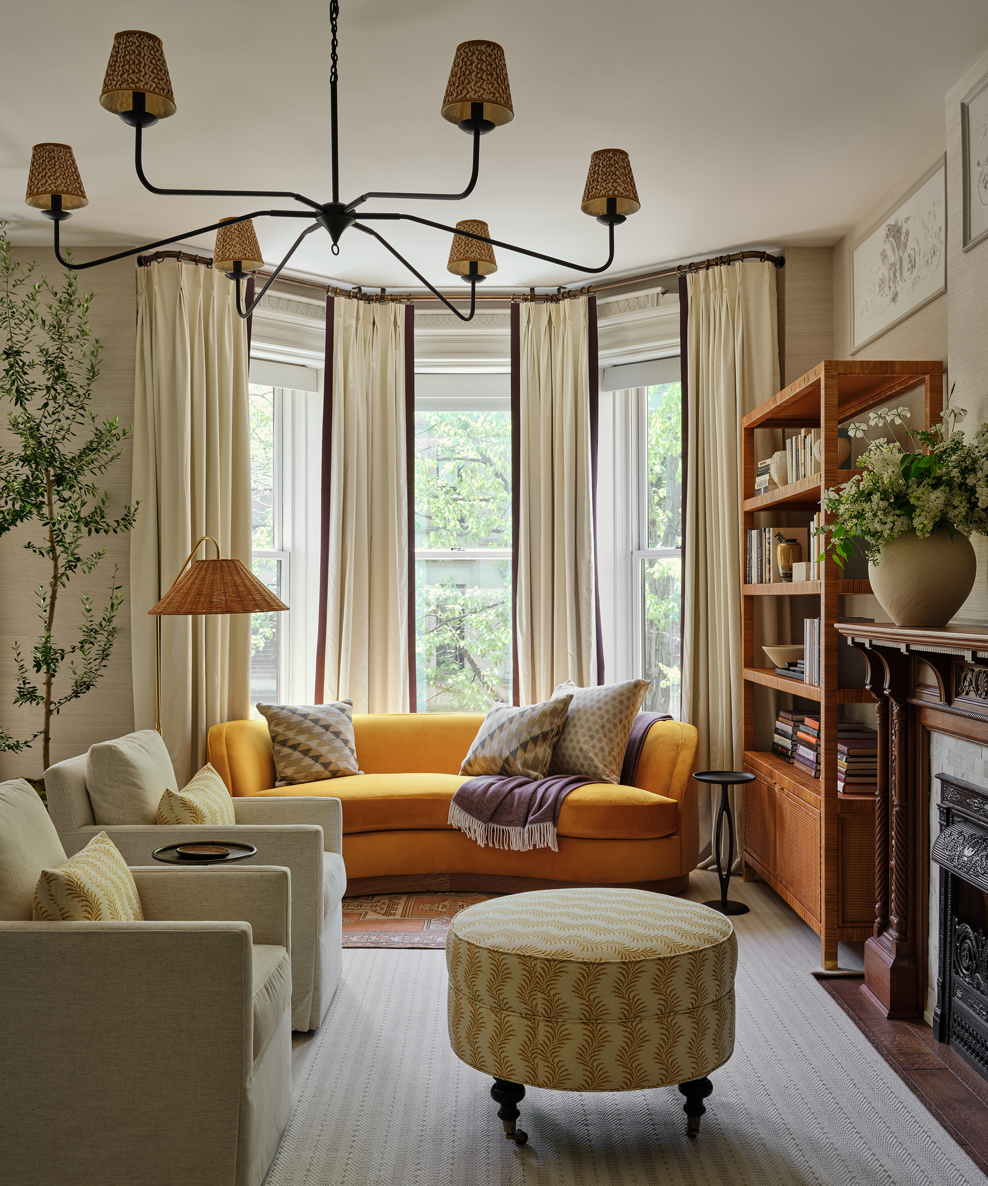 living room with yellow sofa in the bay window and patterned ottoman in the foreground
