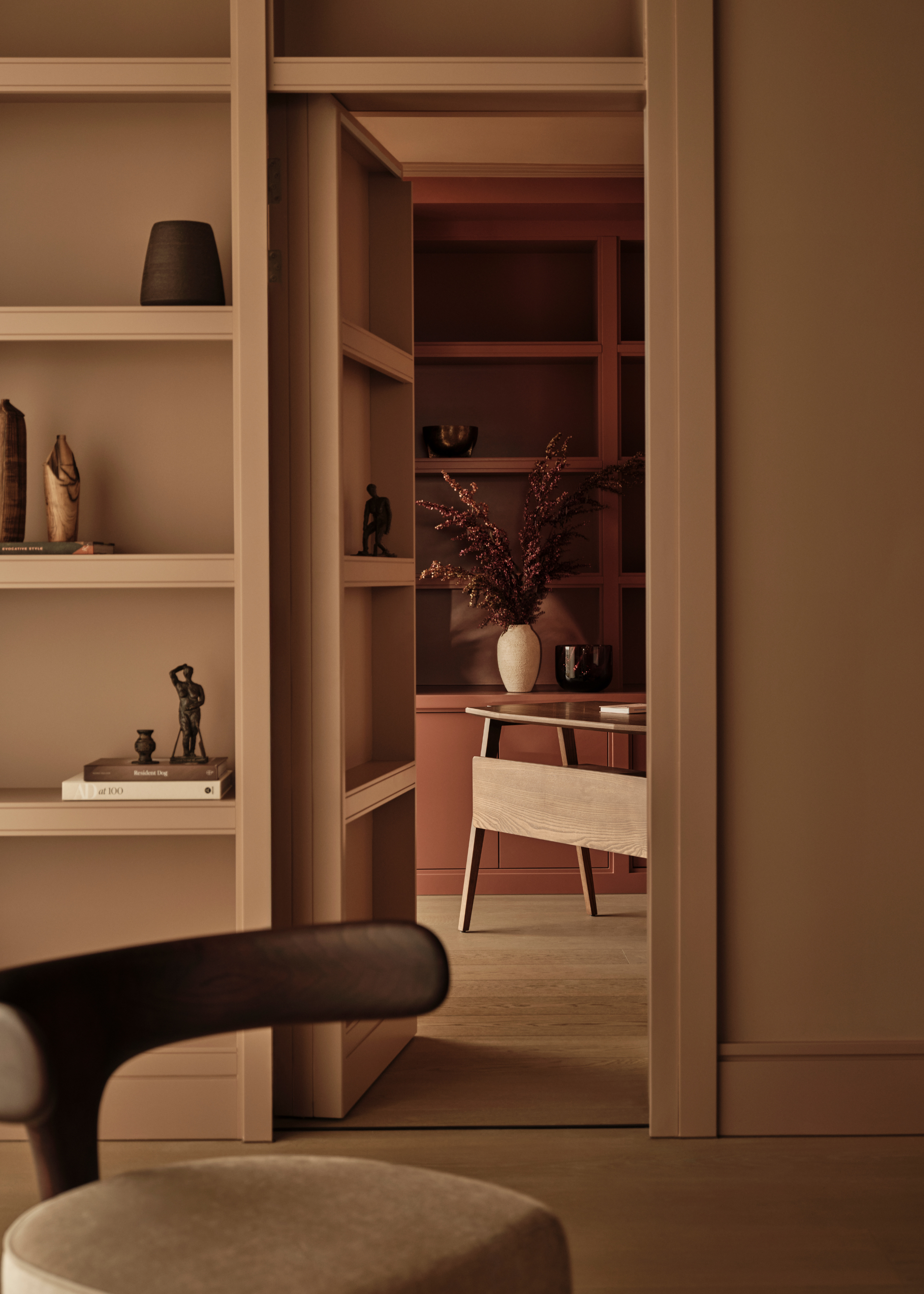 A bookcase conceals a hidden door to a home office with a table and another decorative bookcase painted in a rich orange-brown shade