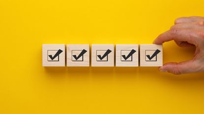 Five wooden blocks lined up against a yellow background with checkmarks on each one.