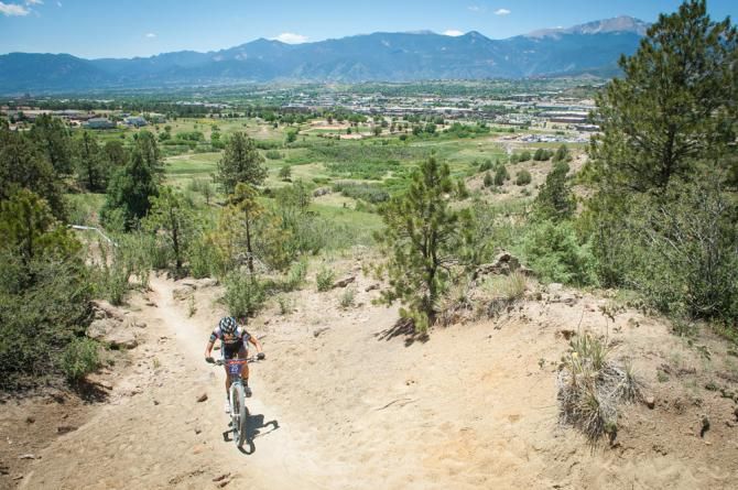 A rider during the elite women's cross country race makes her way up a singletrack section while the City of Colorado Springs, the race venue, and Pikes Peak are ever present.