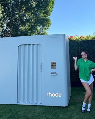 Hailey Bieber poses at a Revolve event wearing a green soccer jersey and white lace bloomers