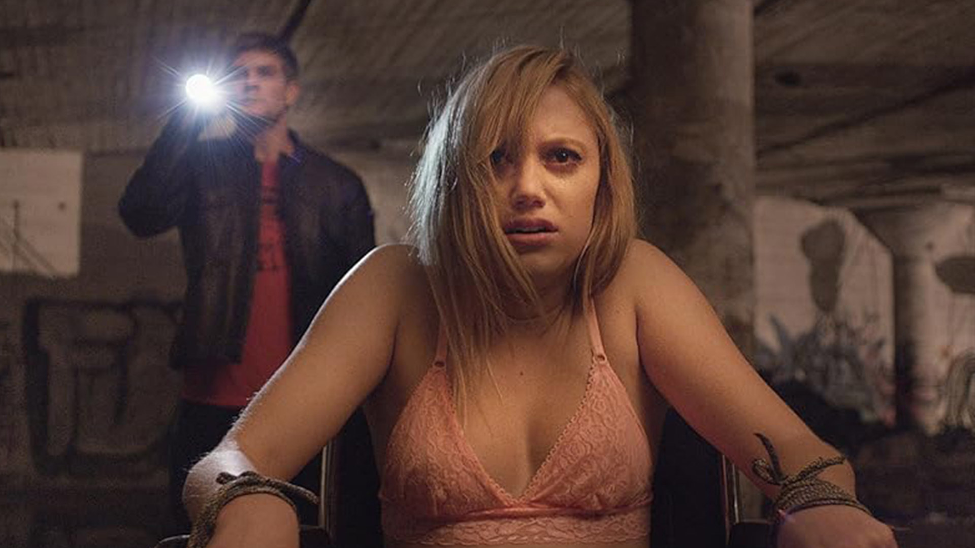 Jay sits in a chair looking scared as Hugh watches on in It Follows