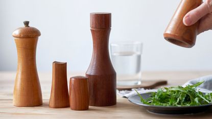 best pepper mill: different pepper mills in wood on a table by a plate of salad