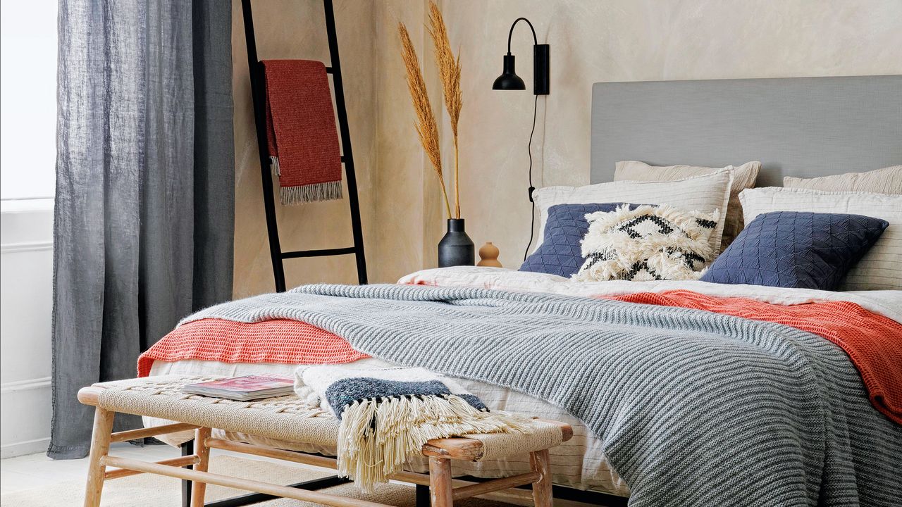 Bedroom with bare plaster walls, black wall light and bed layered with textured bedding