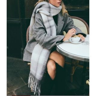 woman sitting at table outside drinking coffee and wearing a grey coat