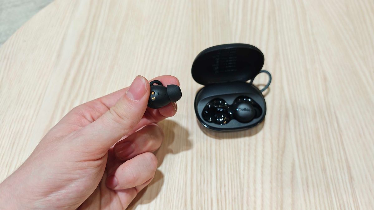 Belkin SoundForm Isolate Buds in orange and in a man's hand, with a wooden table in the background