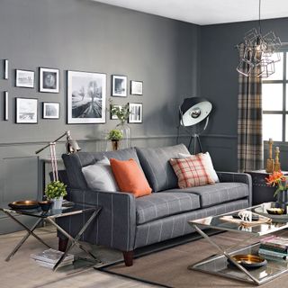 Dark grey living room with dark grey sofa and orange accents. Picture wall above the sofa