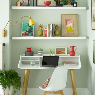 white desk and chair under white shelves with yellow wall lamp