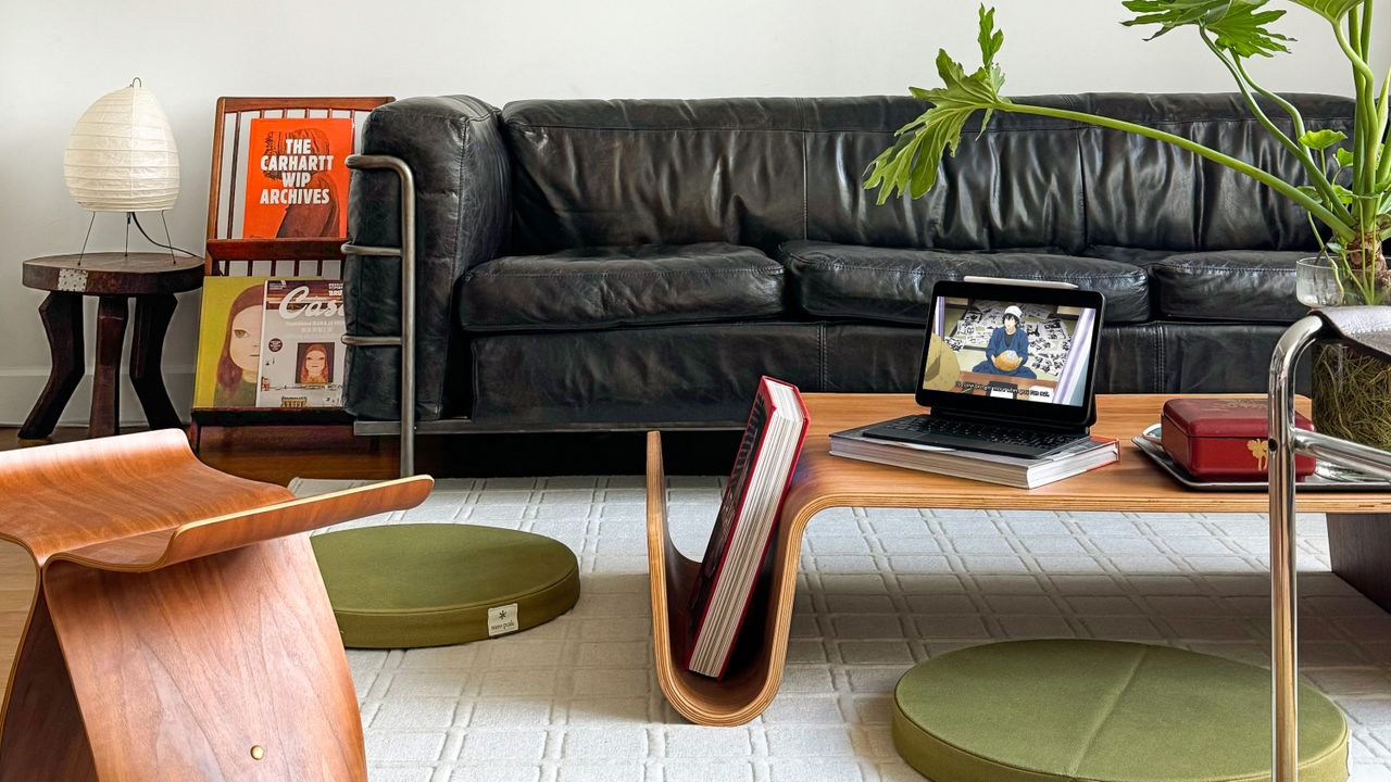 Modern living room with a black leather couch, organically shaped wooden coffee table, and two green floor cushions