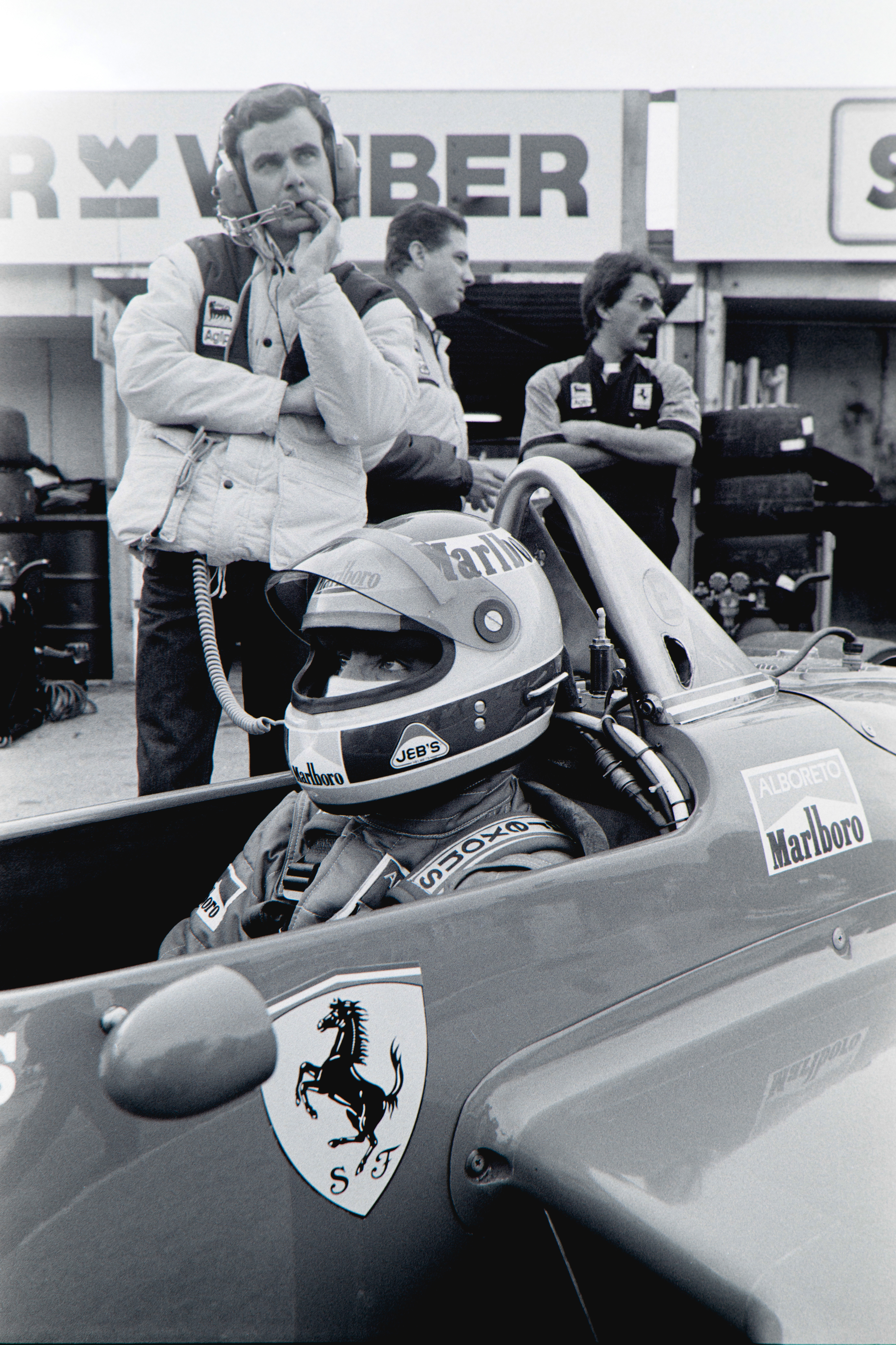 Black and white image of a racing car driver sitting in a Ferrari F1 car in the 1980s