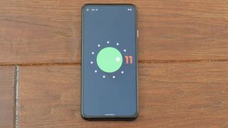 Pixel 4a 5G on dark wood displaying Android 11 easter egg screen