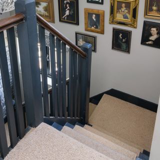 A black-painted staircase with a beige stair runner and a gallery wall