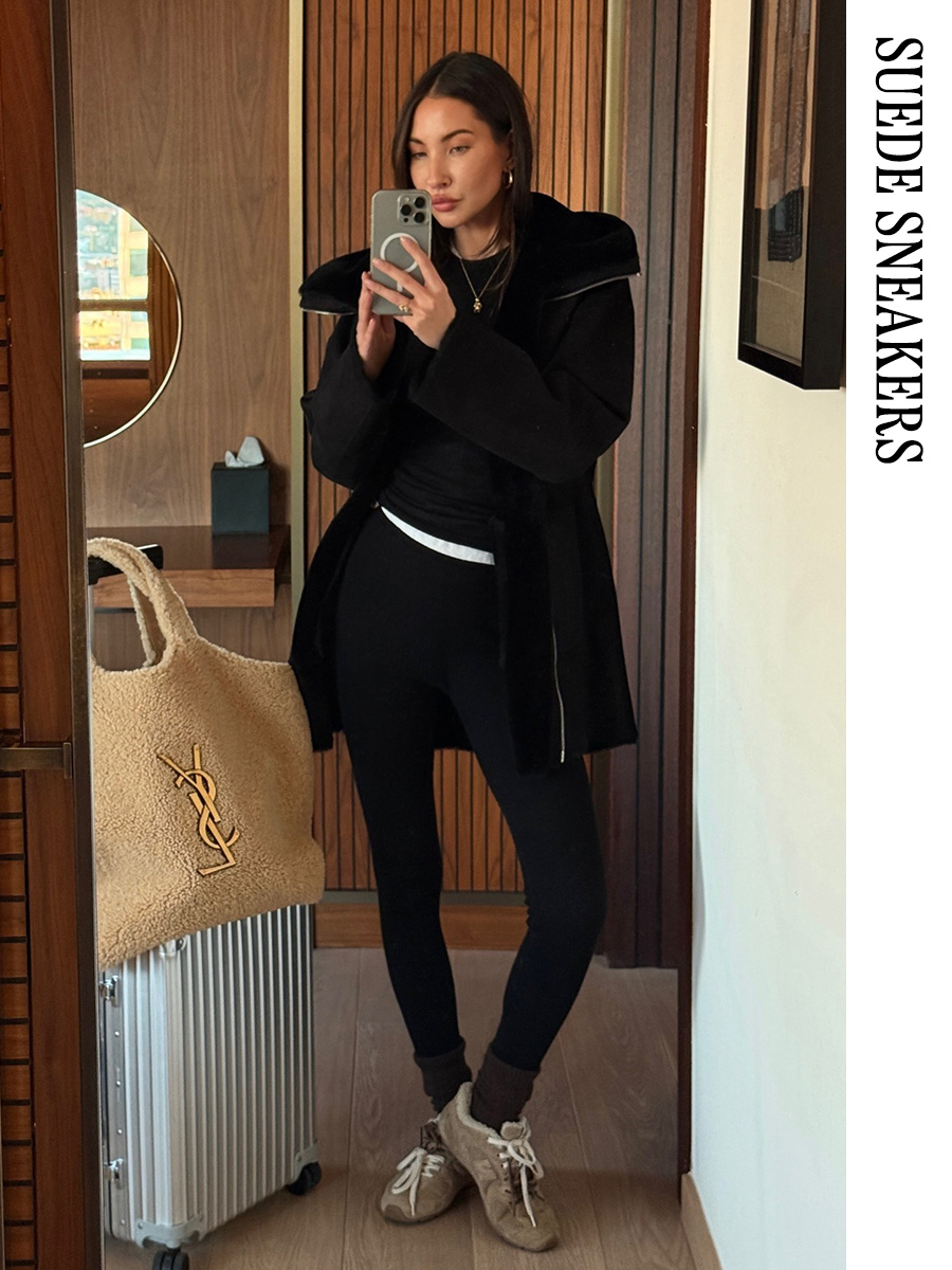 Woman with a suitcase wearing a black jacket, leggings, and suede Miu Miu sneakers