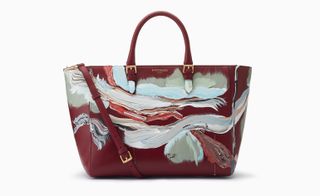 A burgundy handbag with painted sides in shades of light blue.