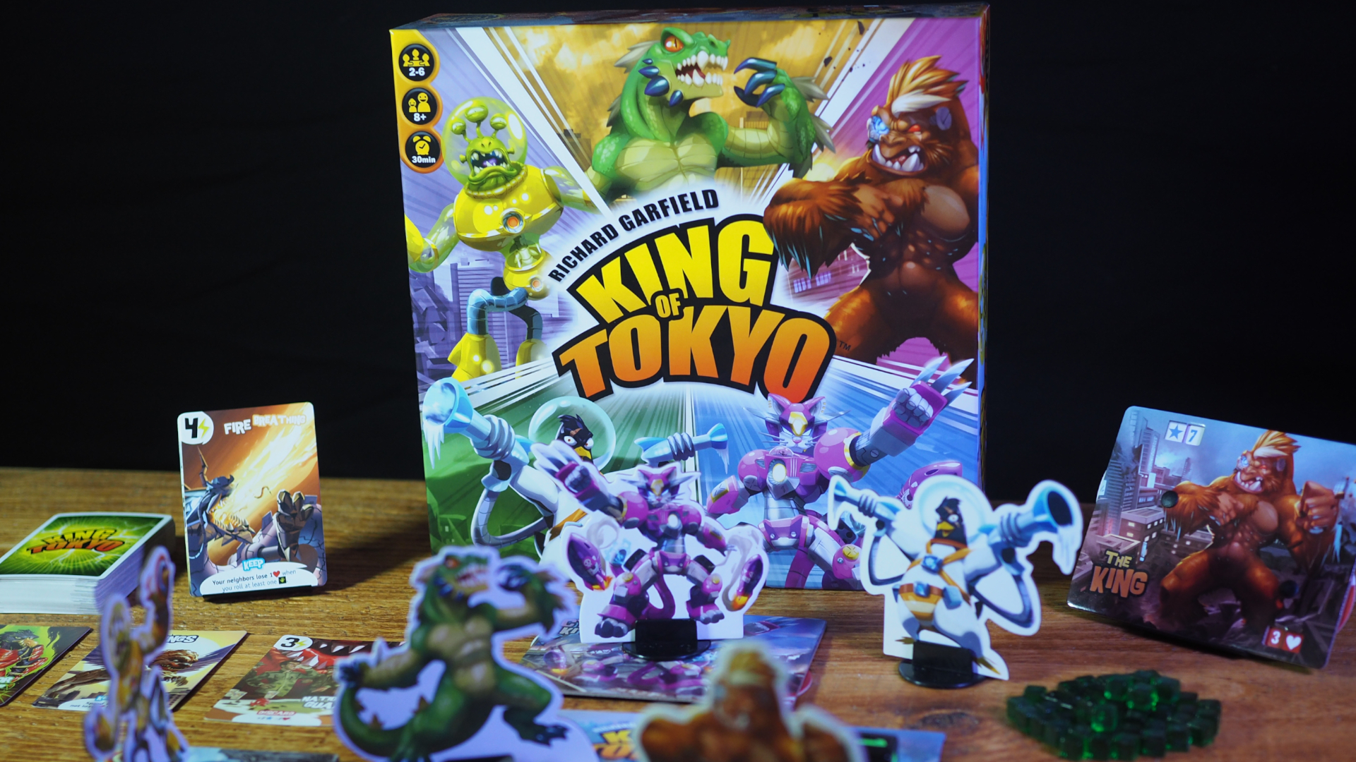 King of Tokyo components, box, and cards on a wooden table against a black background