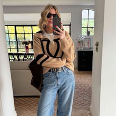 Influencer Emma Thatcher takes a mirror selfie wearing a women's quarter-zip knit over a white t-shirt with blue jeans 