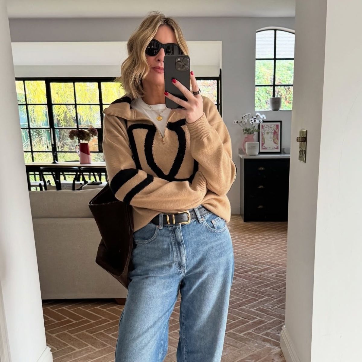 Influencer Emma Thatcher takes a mirror selfie wearing a women's quarter-zip knit over a white t-shirt with blue jeans 