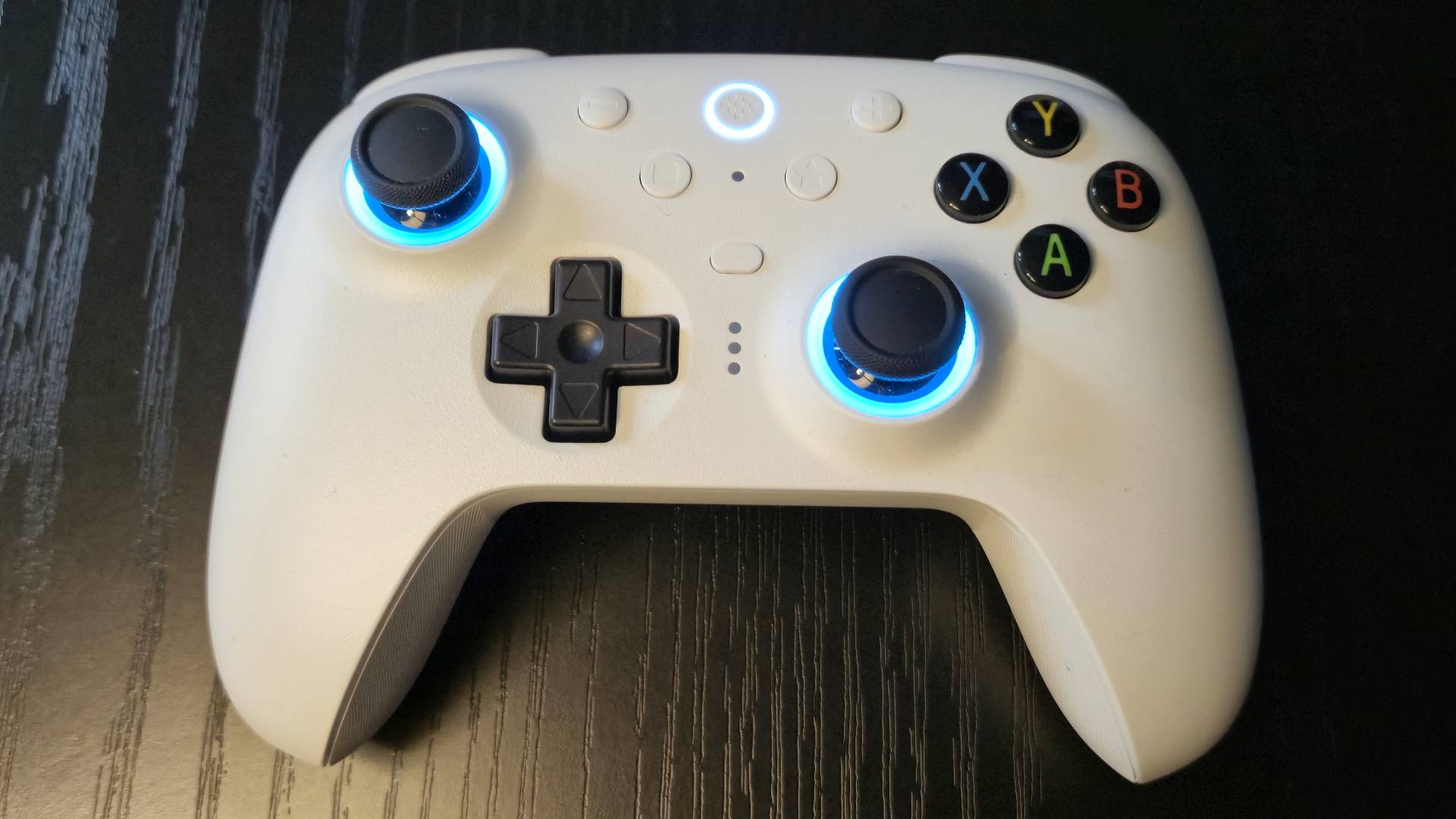 Image of a white controller with blue RGB sticks sitting on a black wooden table.