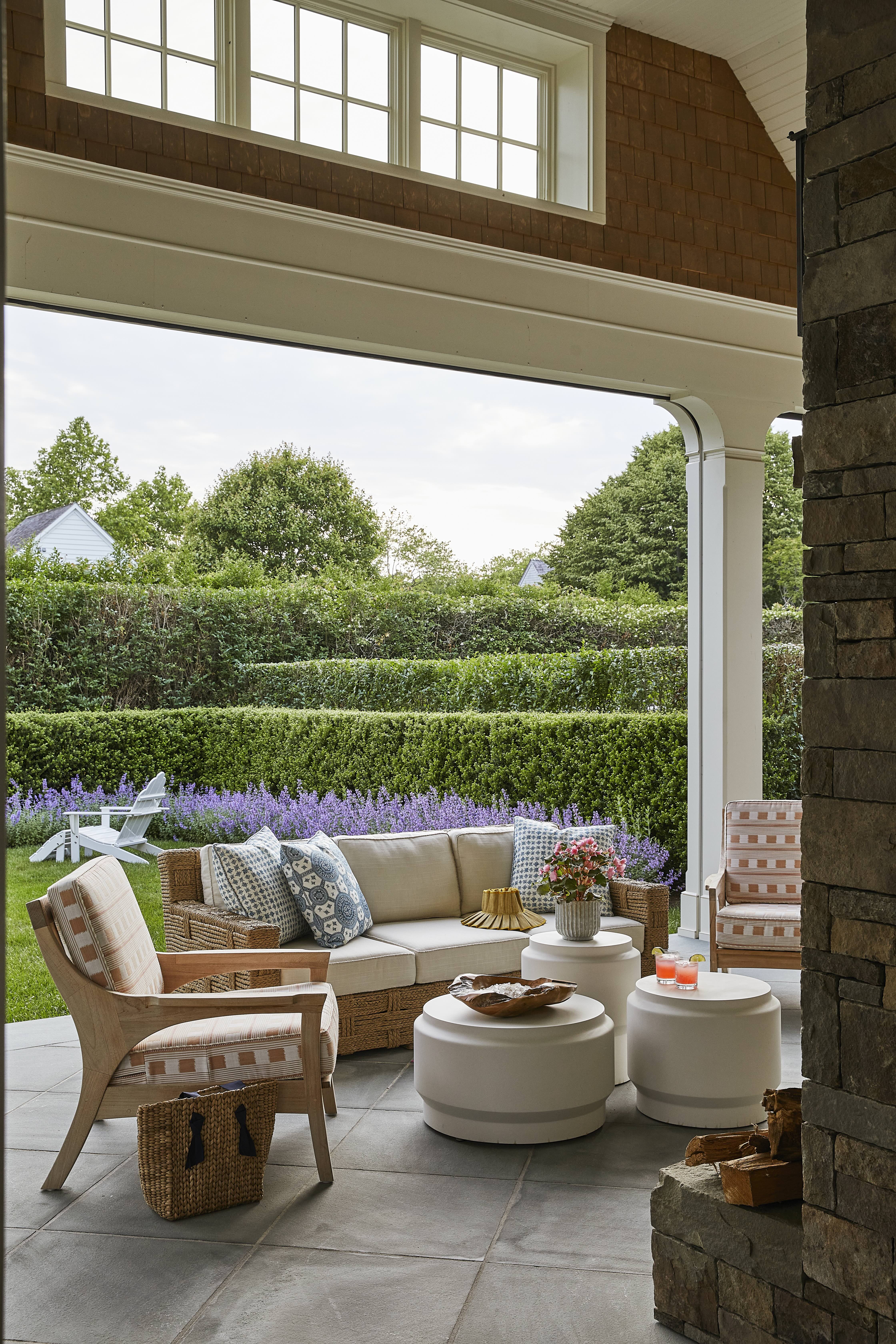 A gorgeous covered back patio with neutral patio furniture and luscious garden hedges.