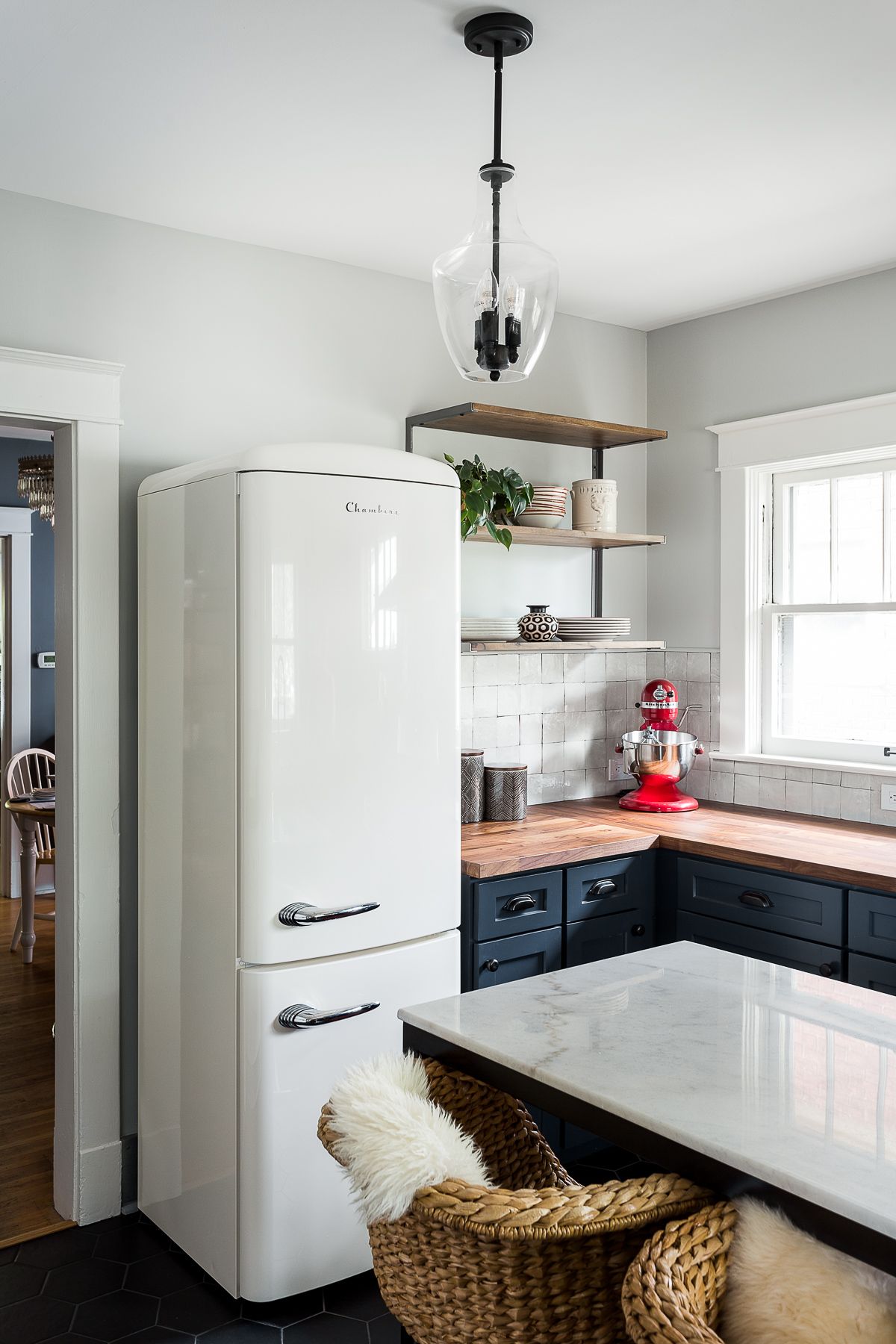 A kitchen with a marble-topped island, jute chairs and a simple pendant light above the island