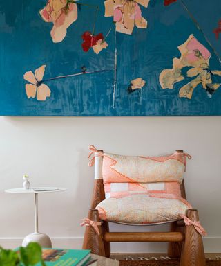 Large colorful floral blue painting above wooden and pink fabric chair