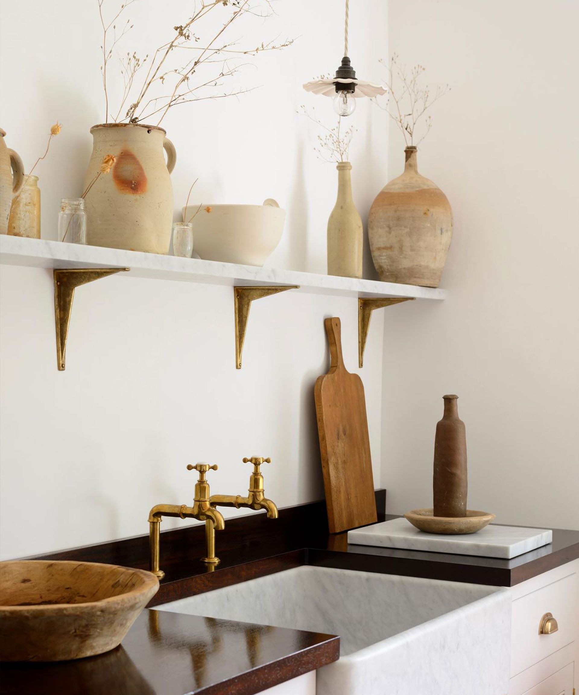 Close up of kitchen shelf decorated with ornaments and vases, wooden boards, low hanging scalloped pendant light