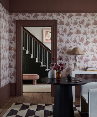 living room with muddy red woodwork, red and ivory wallpaper, wooden floor boards, black and white rug, black side table, white console, white chair, lamps, vases